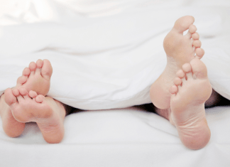 couple's feet poking out of white sheets at bottom of bed. Omaha Mom