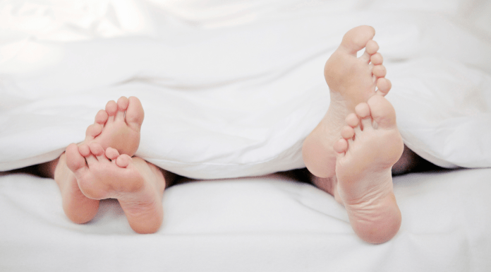 couple's feet poking out of white sheets at bottom of bed. Omaha Mom