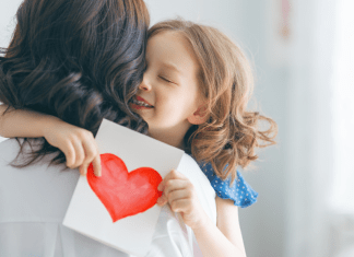 mothers day gifts girl hugging mom and holding white card with a red heart drawn on it