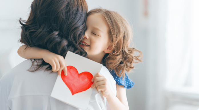 mothers day gifts girl hugging mom and holding white card with a red heart drawn on it